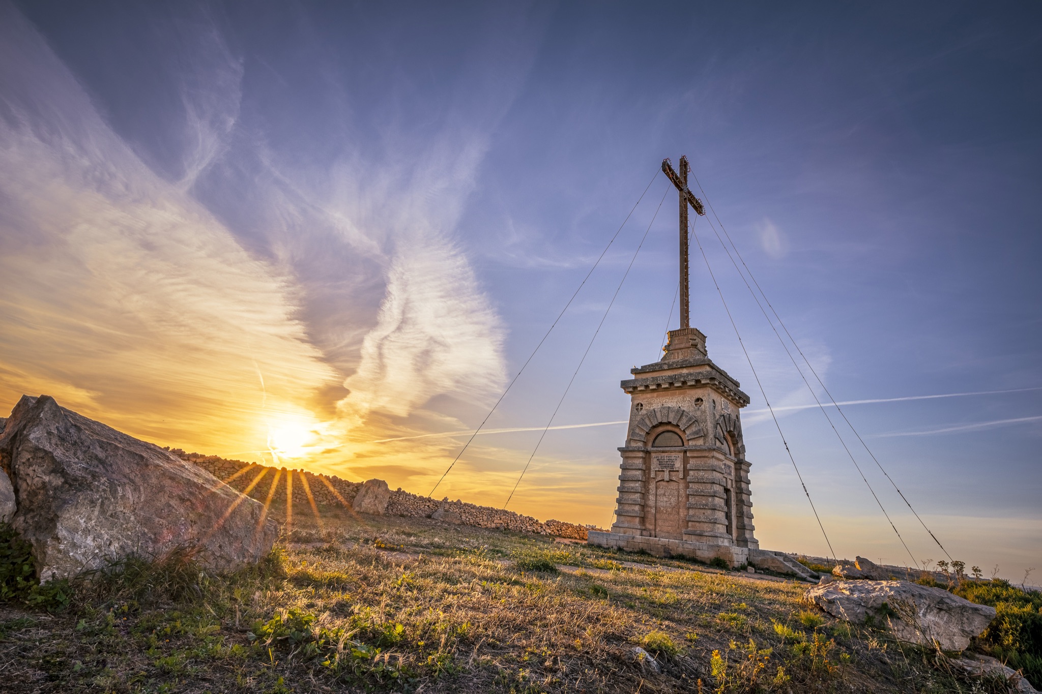 Laferla Cross monument at sunset on a hill in Malta—sun rays behind the cross